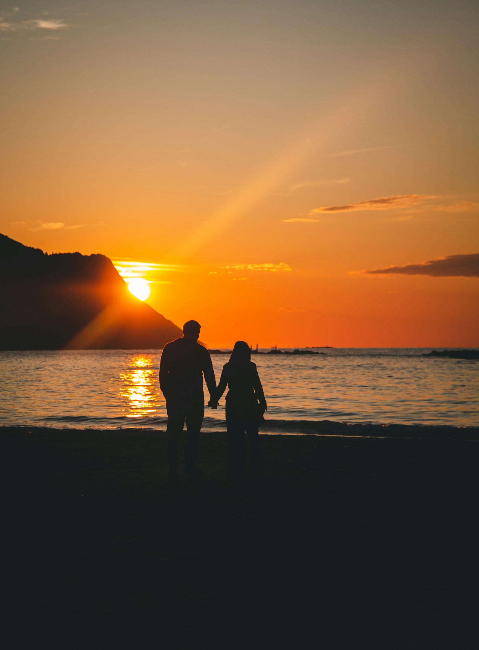 A couple holding hands by the sea at sunset