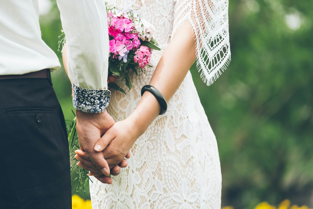 A couple holding hands, with a bridal bouquet and lace dress